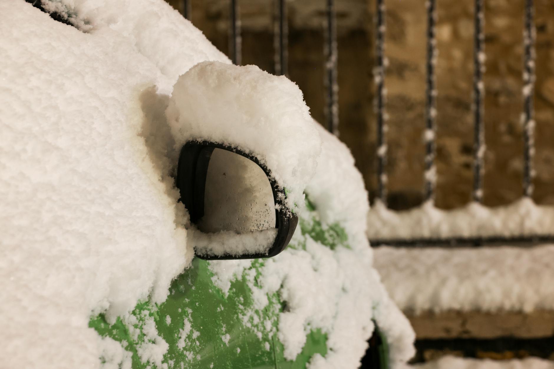 Zamrożone lusterko zielonego auta pokryte śniegiem zimą