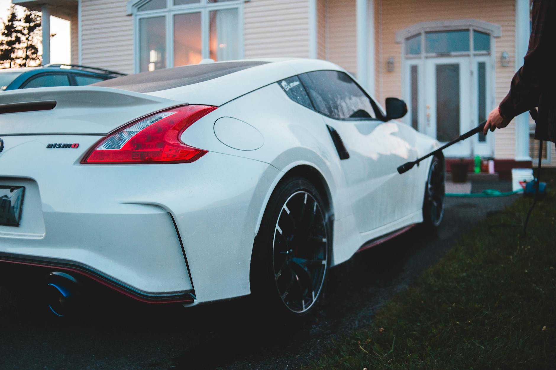 Biały Nissan 370Z myty wodą z węża podczas domowego detailingu