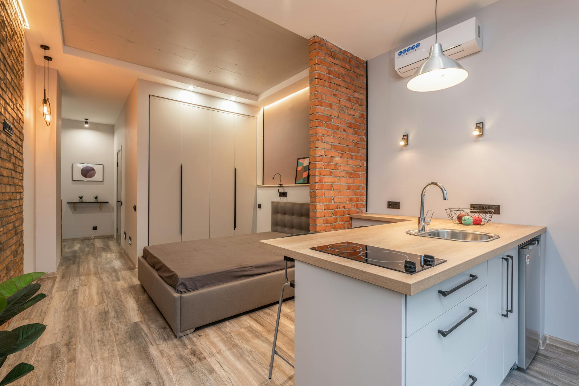 Jak urządzić funkcjonalny mikroapartament: praktyczne rozwiązania dla małych przestrzeni Mikroapartament z aneksem kuchennym i sypialnią za ceglaną ścianką
