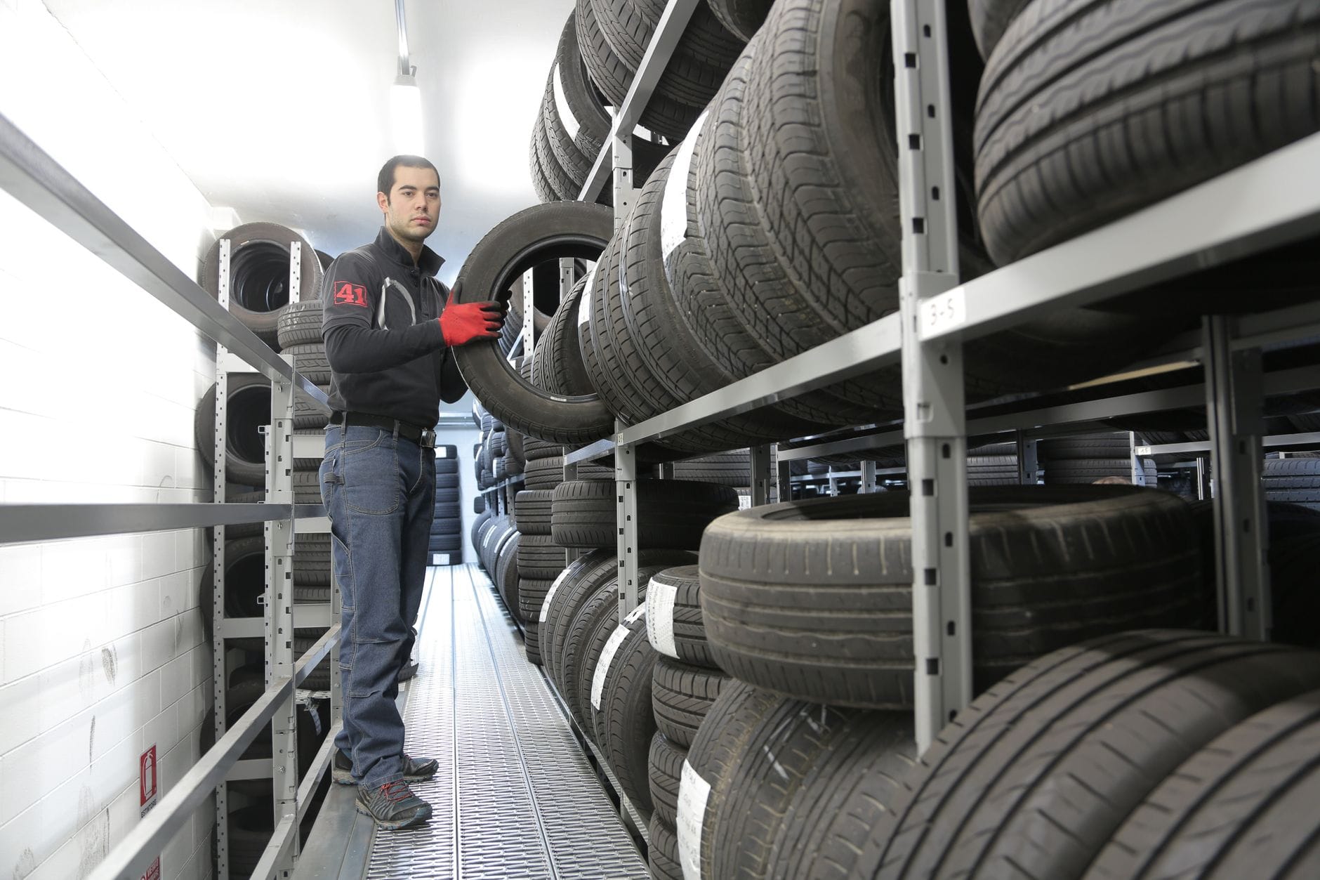 Mechanik odkłada oponę na regał w magazynie z oponami