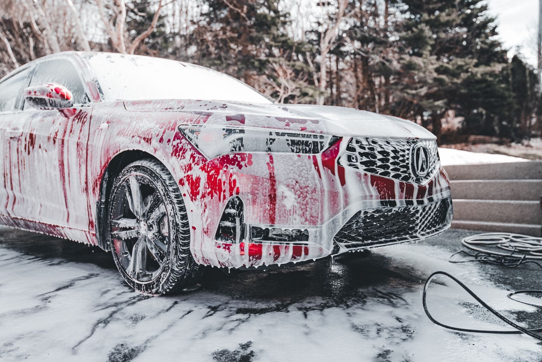 Czerwone auto pokryte pianą podczas mycia na zewnątrz w dzień
